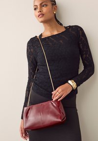 Dieprode leren handtas met een nonchalant ontwerp, afgewerkt met een dunne gouden kettingriem, gecombineerd met een zwart kanten top met lange mouwen.