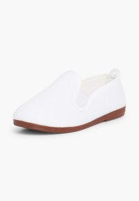 Chaussure blanche à enfiler avec une semelle basse marron et un panneau latéral élastique, conçue pour un port facile et confortable.
