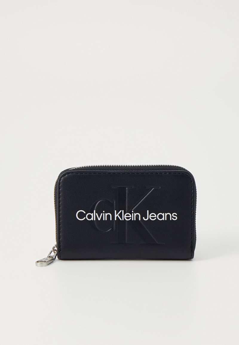 Carteira preta com fecho de correr, feita de material sintético, com o logótipo em relevo "CK" e "Calvin Klein Jeans" em texto branco na frente.