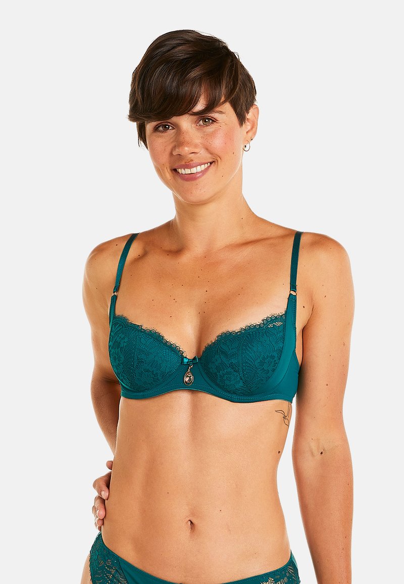 Soutien-gorge en dentelle teal avec armatures, bonnets rembourrés, bretelles ajustables et un pendentif décoratif central. Motif floral sur le bord en dentelle.