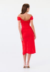 Robe rouge décolletée avec un corsage ajusté et une longueur de jupe mi-longue, présentant un motif floral texturé et une fermeture éclair dissimulée au dos.