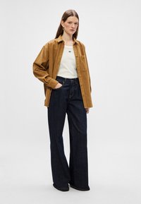 Brown corduroy shirt, white top, and dark blue wide-leg jeans. The shirt features a pocket and button front. The fabric is textured and soft.