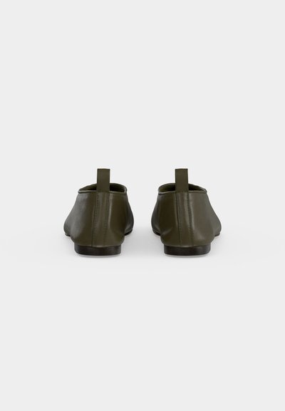Paire de chaussures slip-on vert olive avec semelles plates noires, vue de dos sur un fond uni clair.