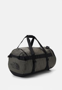 Sac de sport vert foncé de forme cylindrique, en tissu durable, avec des poignées noires et un logo. Comprend des boucles et une surface texturée.