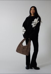 Svart tröja med vitt blommönster, kombinerad med utsvängda svarta byxor och en brun väska med leopardmönster. Tjocka svarta kängor fulländar outfiten.