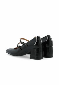 Zapatos de charol negros de tacón alto con punta afilada, dos correas en el tobillo con hebillas circulares y tacones cuadrados gruesos.