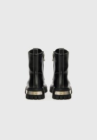 Melnas ādas potītes zābakus ar masīvu, rievotu zoli un metālisku papēža akcentu. Iezīmē sudraba rāvējslēdzējs un kontrastējoša šuvju apdare.