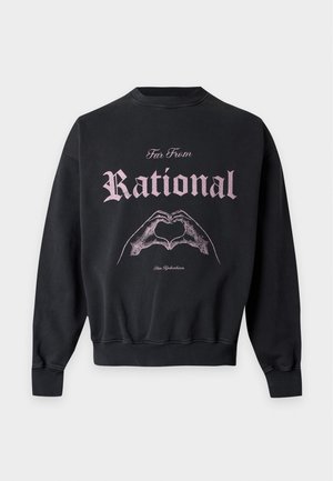 Jonge man met een zwarte sweatshirt met tekst en een hand-hart grafiek, bruine wijde cargobroek en zwarte sneakers.