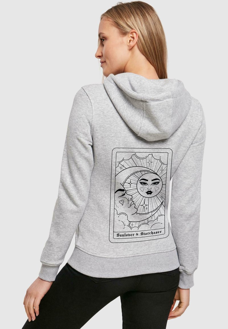 Sudadera con capucha gris que presenta un diseño gráfico de un sol y una luna en la parte posterior, con contornos y detalles en negro, en un corte relajado.