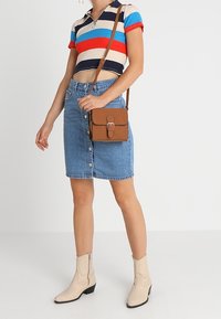 Pasiasta krótka koszulka polo w kolorach czerwonym, niebieskim i kremowym; niebieska spódnica z denimu zapinana na guziki; brązowa torba na ramię; beżowe kowbojskie buty z przeszyciami.