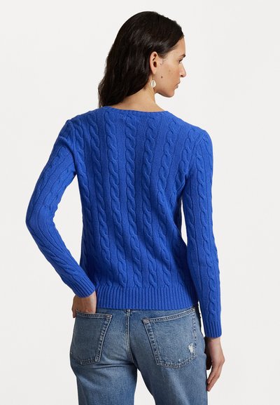 Blå strikket kabelgenser med lange ermer, ribbet kant og strukturert mønster. Brukt med lyseblå slitte denimjeans.