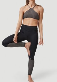 Černé sportovní legíny s síťovými detaily a vysokým pasem, kombinované s vzorovaným topem na halter. Stretchový materiál, těsný střih.