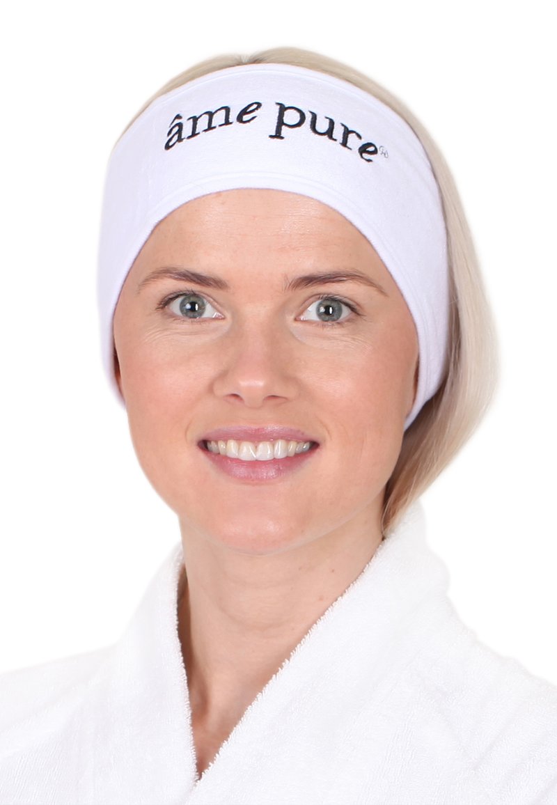 Weißes Stirnband mit schwarzem Text "âme pure", getragen von einer Person mit hellblonden Haaren, die lächelt, in einem weißen Gewand vor einem einfarbigen Hintergrund.