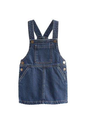 Denim overal šaty s nastaviteľnými ramienkami, vreckami a zlatými gombíkmi, nosené cez čierno-biele pruhované tričko s dlhým rukávom a tmavé topánky.