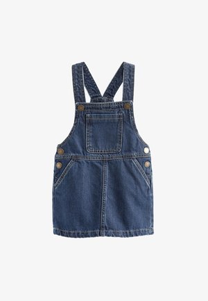 Denim overallskjorte med justerbare stropper, lommer og guldknapper, båret over en sort og hvid stribet langærmet skjorte og mørke støvler.