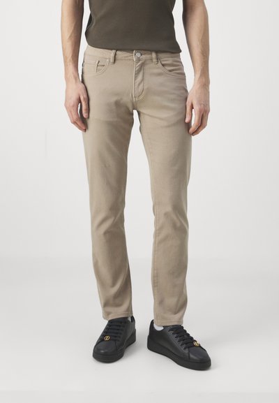 Beežid denim püksid kitsas lõikega, viie tasku ja nupukinnitusega, koos mustade tossudega. Sile tekstuur, minimalistlik disain.