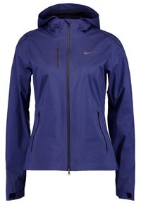 Veste imperméable à capuche bleu marine avec fermeture éclair intégrale à l'avant, deux poches latérales zippées, une poche zippée sur la poitrine, et logo Nike sur le côté gauche de la poitrine.