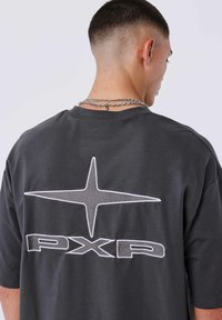 Camiseta de gran tamaño color gris oscuro con un gran logotipo de estrella blanca y el texto "PXP" en la parte posterior. Tela suave, mangas cortas, corte relajado.
