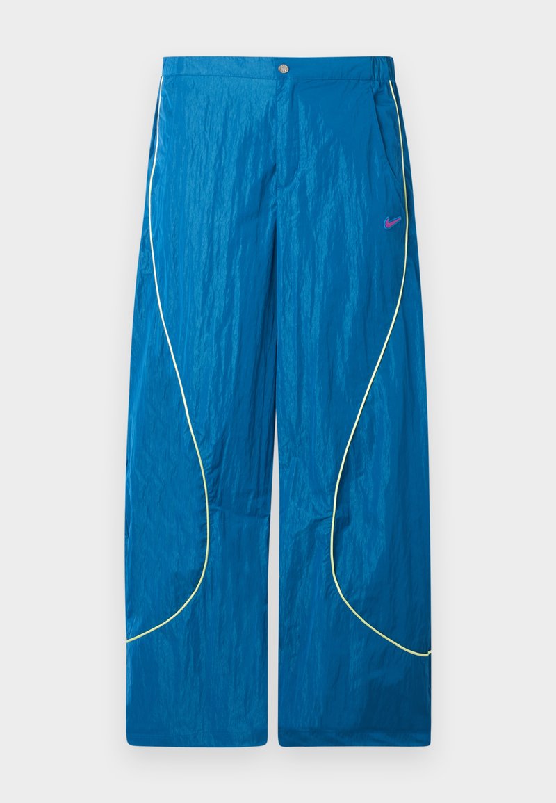 Pantaloni sportivi blu a gamba larga con dettagli in piping giallo riflettente e piccolo logo Nike rosa sul lato destro della coscia, chiusura con bottoni e cerniera.