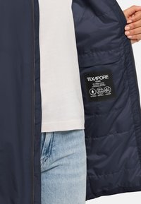 Giacca blu navy con interno trapuntato, etichetta Texapore visibile. Presenta un esterno liscio e una zip frontale completa.