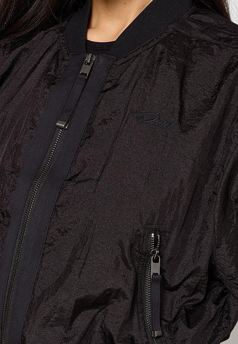 Schwarze Bomberjacke aus glänzendem Stoff, mit geripptem Kragen und Reißverschluss vorne sowie seitlichen Taschen; dezentes Logo auf der Brust gestickt.