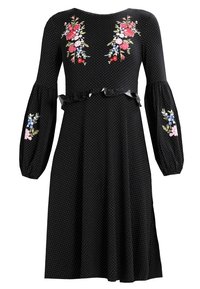 Vestido negro con lunares blancos, mangas largas abullonadas, bordado floral en rojo, rosa y azul, y un detalle fruncido en la cintura.