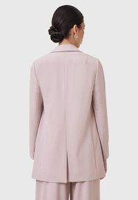 Blazer rosa realizzato in tessuto liscio, con colletto a punta, maniche lunghe e uno spacco centrale sul retro per una vestibilità su misura.