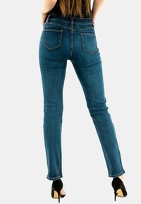 Jeans de mezclilla azul delgados con una cintura de altura media, diseño de cinco bolsillos y bolsillos traseros cosidos, combinados con tacones altos negros.