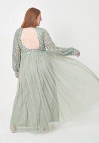 Langes grünes Kleid mit einem enganliegenden, mit Pailletten besetzten Oberteil und einem fließenden, transparenten Rock. Der offene Rücken und die langen Ärmel schaffen eine elegante Silhouette.