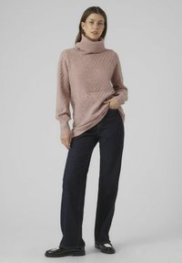 Light pink turtleneck sweater with a textured diamond pattern, paired with dark blue wide-leg jeans and black shoes with a glossy accent.