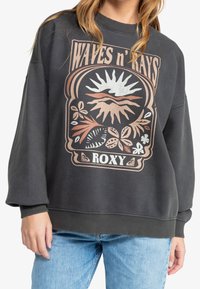 Sudadera gris oscura con cuello redondo, que presenta un gran diseño gráfico en tonos terrosos que incluye elementos de sol y florales.