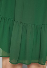 Zielona, warstwowa sukienka z lekkiego materiału. Posiada falbankowy dół o miękkiej fakturze oraz gładką górną część.