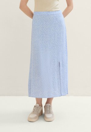 Jupe midi bleu clair avec motif floral blanc et fente latérale portée avec des baskets beiges et un haut crème, montrée du milieu du torse vers le bas.