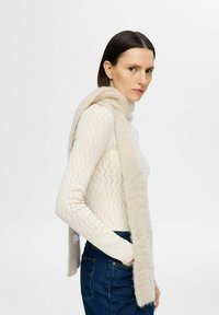 Ljusbeige sjal med en mjuk, fluffig textur hängande över en krämfärgad, stickad tröja med ett diagonalt mönster.