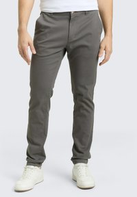 Γκρι, εφαρμοστή παντελόνια με λεία υφή, διαθέτει φερμουάρ μπροστά, θηλιές για ζώνη και μία κουμπωτή κλειδαριά. Φορεμένα με λευκά αθλητικά παπούτσια.