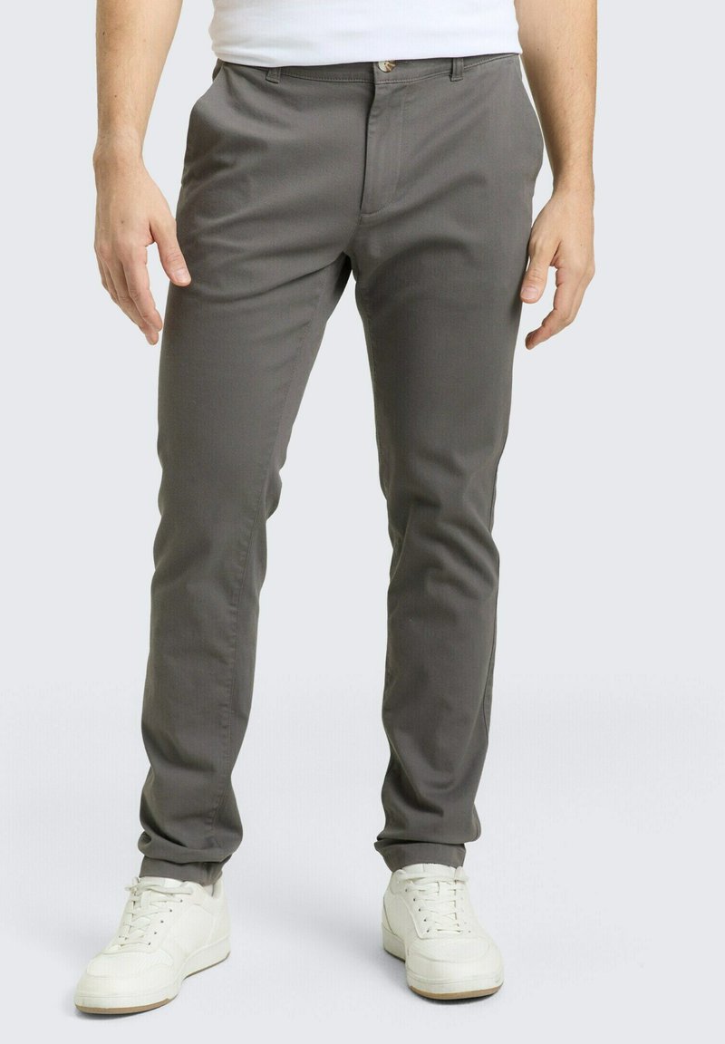 Γκρι, εφαρμοστή παντελόνια με λεία υφή, διαθέτει φερμουάρ μπροστά, θηλιές για ζώνη και μία κουμπωτή κλειδαριά. Φορεμένα με λευκά αθλητικά παπούτσια.