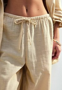 Linnebyxor i en ljus beige färg med elastisk midja och snörning. Mjuk textur med små variationer i vävningen.