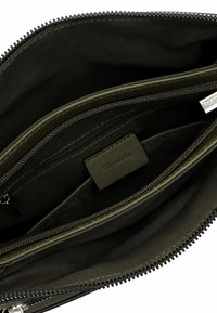 Pochette nera con zip e multiple tasche, foderata in tessuto scuro, con un dettaglio verde oliva e una piccola etichetta all'interno.