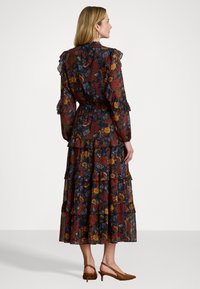 Ziedu maxi kleita ar frillēm pie piedurknēm, pakāpenisku dizainu un pielāgotu jostu. Iezīmē tumšu fonu ar sarkaniem, oranžiem un ziliem ziedu rakstiem.