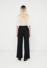 Blouse blanche à pois noirs associée à un pantalon large noir, mettant en avant une texture douce et une coupe décontractée, vue de dos.