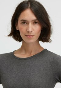 Gray, short-sleeve shirt with a round neckline, made of smooth, fitted fabric. The model has shoulder-length hair and neutral makeup.