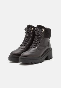 Bottes noires en cuir à la cheville avec une plateforme épaisse, un revers en fourrure, des œillets en métal et de grosses lacets. Semelle en caoutchouc texturée avec des stries.