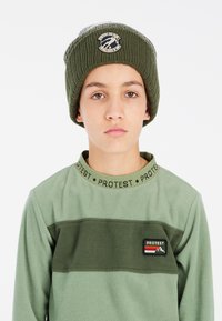 Žalias ribotas kepurė su logotipu ir žalias fliso viršus su horizontaliu dryžiu bei ženkleliu ant krūtinės. Minkšta tekstūra, kasdieniškas dizainas.