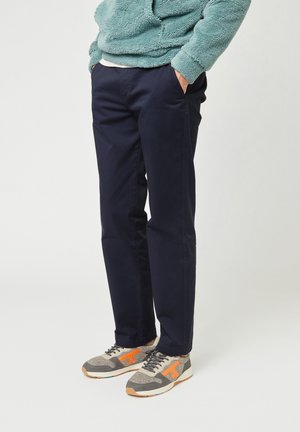Chino blu navy con una vestibilità dritta, realizzati in cotone. Abbinati a sneakers in mesh grigio con accenti arancioni e una superficie testurizzata.