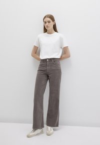 White short-sleeve T-shirt paired with high-waisted, wide-leg gray corduroy pants, worn with light-colored sneakers. Simple and modern design.