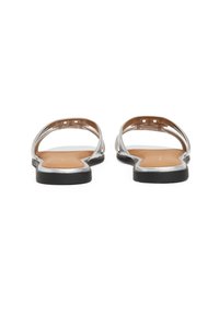 Flade sandaler med sølvstropper, tan sål og sort ydersål. Åben bagside-design med udsparingsdetaljer på stropperne, der viser en minimalistisk stil.