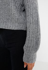 Gray knitted sweater with a textured rib pattern, featuring a loose fit and wide sleeves. The material appears soft and chunky.