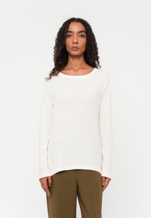 Long-sleeve cream shirt in soft fabric with a wide neckline, side slits, and a relaxed fit, paired with olive green trousers.