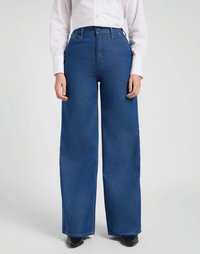 Calças de ganga azuis de perna larga com uma cintura alta, apresentando passantes para cinto e fecho com botão, combinadas com uma camisa branca de mangas longas.