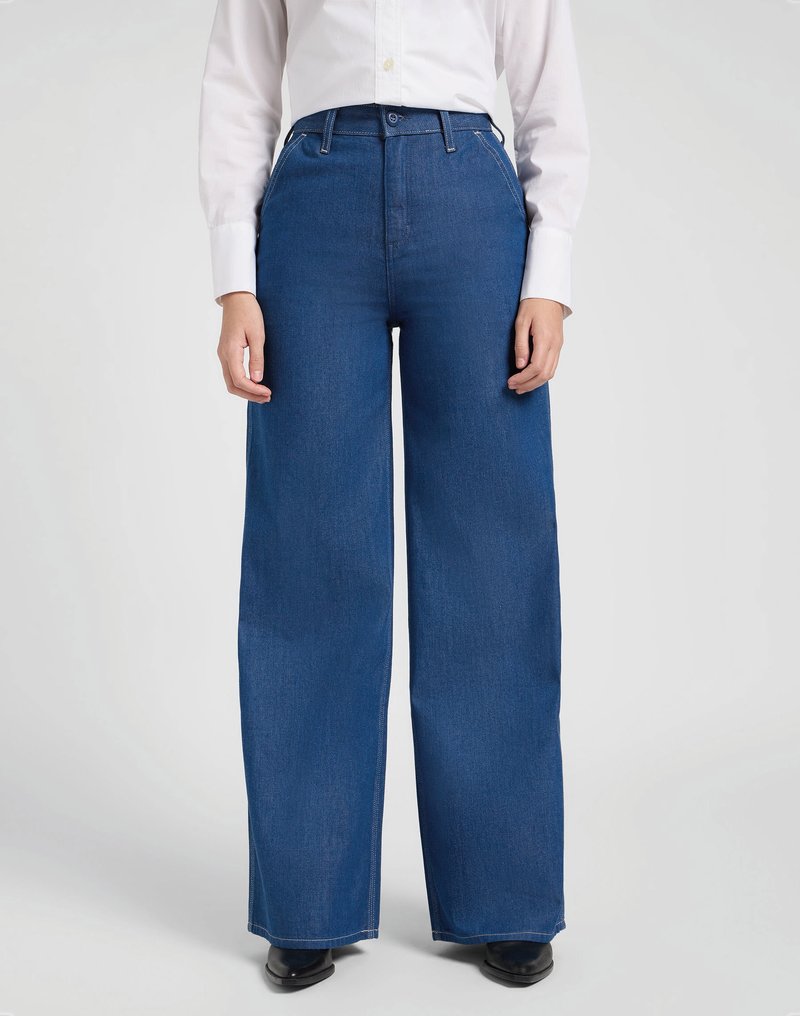 Calças de ganga azuis de perna larga com uma cintura alta, apresentando passantes para cinto e fecho com botão, combinadas com uma camisa branca de mangas longas.